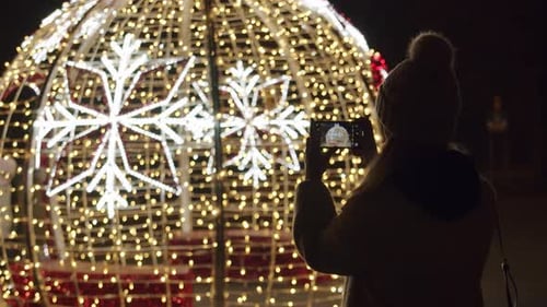 Woman Photographs Christmas Decoration at Night with Phone