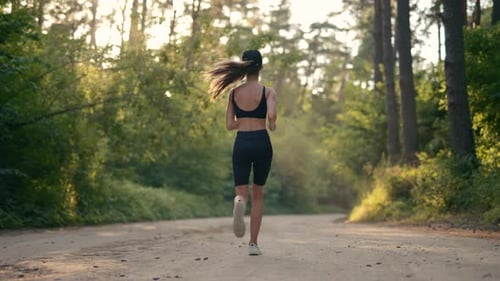 A Young Woman Runner is Listening to Music in Earphones and Training in Summer Forest