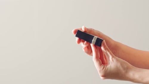 Weibliche Hände halten Lippenstift vor weißem Hintergrund