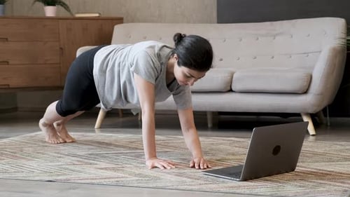 Close Up A Young Indian Woman Does A Plank Exercise, Does Yoga Online At Home In A Bright Room