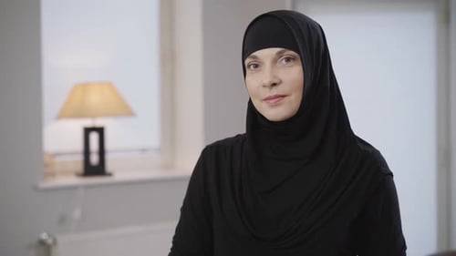 Mittlere Aufnahme einer schönen muslimischen Frau in schwarzem Hijab, die in die Kamera blickt und lächelt. Süße Dame mit
