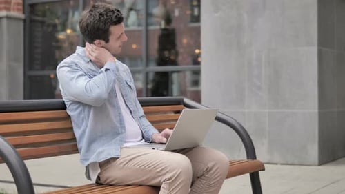 Man Works on Laptop and Massages Neck Outdoors
