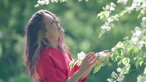 Happy Woman in Blooming Garden in Springtime Laughing and Playing with Branch of Tree with Blossoms