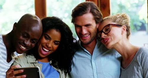 Smiling Friends Looking at Smartphone Together Indoors