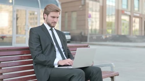 Joven empresario señalando a la cámara mientras está sentado en un banco al aire libre