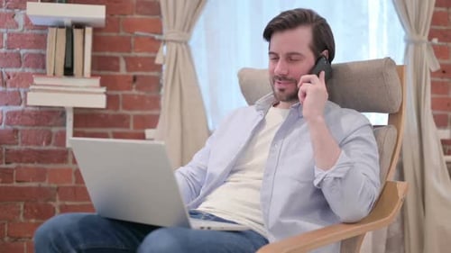 Young Adult Talking on Phone While Using Laptop