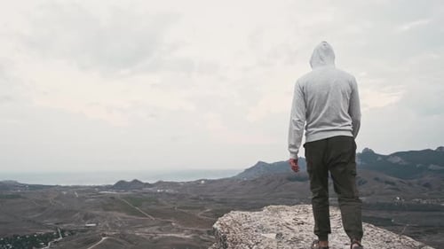 Happy Man Climbing on Top of Cliff and Raises Hand His Fist Up