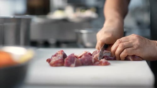 Cook Prepares Meat by Cutting It in Kitchen