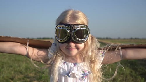 Porträt eines Mädchens im Bild eines Flugzeugpiloten mit Pappflügeln