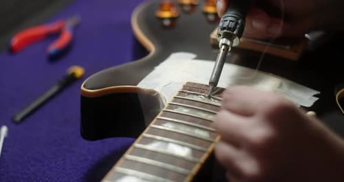 Luthier calienta los trastes de la guitarra soldando el hierro antes de iniciar los preparativos para el reemplazo de los trastes