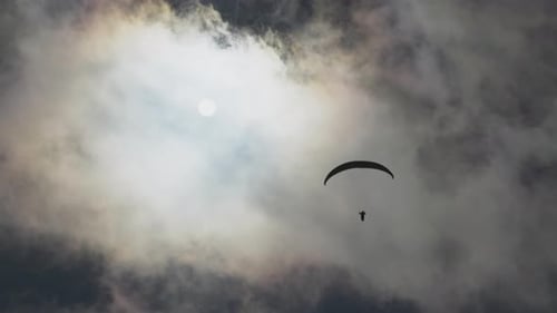 Gleitschirmfliegen Abenteuersport gegen strahlende Sonne am bewölkten Himmel