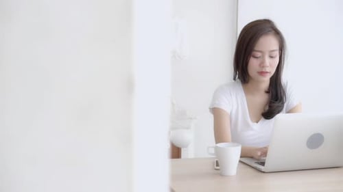 Schöne junge freiberufliche asiatische Frau, die lächelt und am Schreibtisch arbeitet und am Laptop-Computerjob tippt.