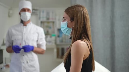 Doctor with Syringe Walking From Background to Young Woman Sitting in Vaccination Clinic