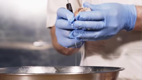 Gloved Hands Cracking an Egg into Bowl