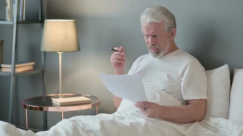 Man Looks at Documents in Bed