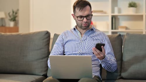 Man Using Smartphone and Laptop on Gray Couch