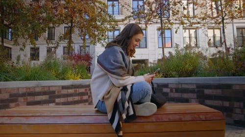 Woman Using Smartphone on Bench in Urban Setting