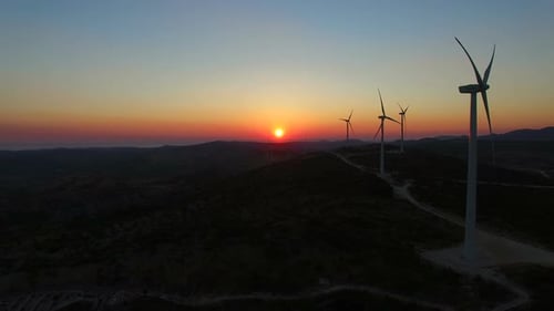 Luftaufnahme von Windmühlen mit langsam rotierenden Flügeln bei Sonnenuntergang