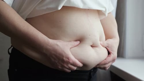 Aged Woman Compresses Skin on Abdomen Checking Fat Excess