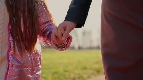 Mom hold child by hand close up outdoors. Two female persons girl and woman walking at park