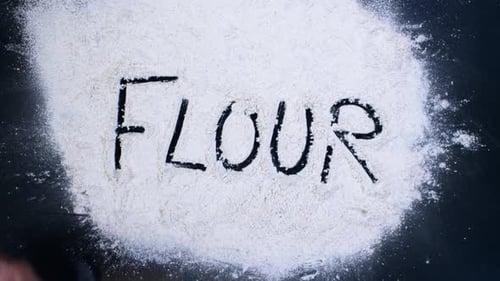 Hand Writes the Word Flour in Pile of Flour