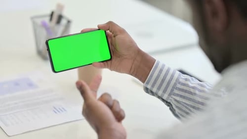 Rear View of African Man Looking at Smartphone with Green Chroma Key Screen