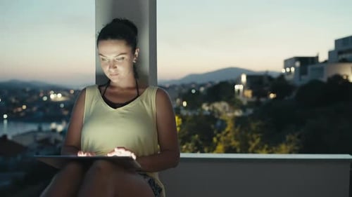 Young Woman Using Tablet on Balcony at Night