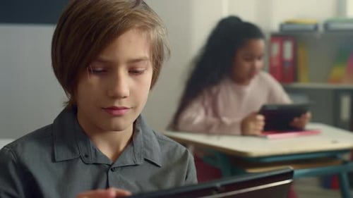 Lächelnder Schüler sitzt am Schreibtisch mit digitalem Tablet in der Grundschule