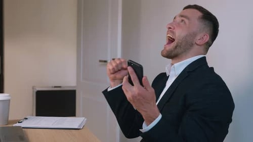 Excited Businessman Receiving Good News on Phone at Desk
