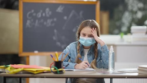 Portrait of Overwhelmed Junior High Schoolgirl in Covid Face Mask Holding Head in Hands Sighing