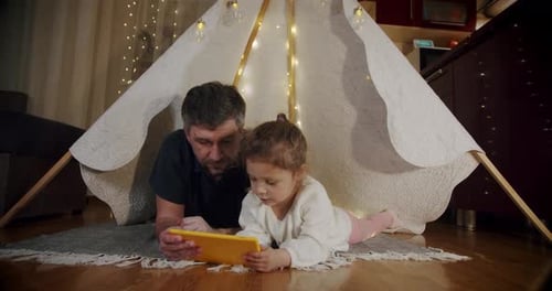 Father and Child Playing Tablet in Lit Tent