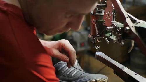 Männlicher Schuhmacher in roter Kleidung repariert Schuhe im Licht einer Lampe
