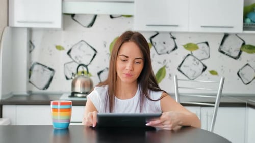 Woman Uses Tablet and Drinks Coffee in Kitchen