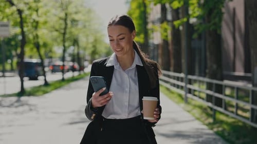 Business Woman Walking on City Street with Cup of Coffeetogo While and Using Modern Smartphone