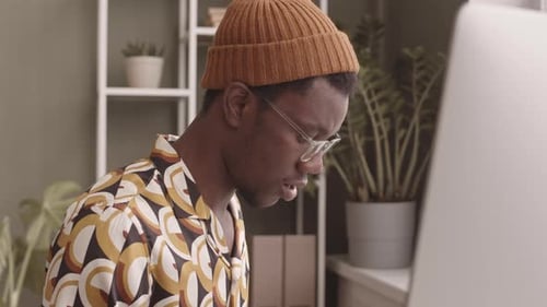 Black Man in Beanie Hat Typing on Computer in Office