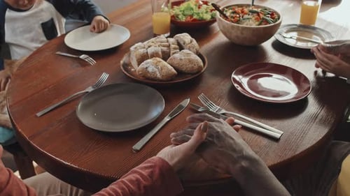 Family Holding Hands Around Table Before Meal