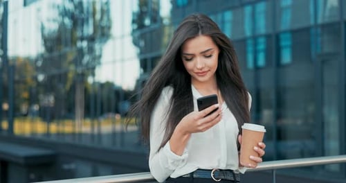 Businesswoman Using Smartphone and Holding Coffee Outdoors