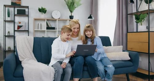 Madre y su hijo e hija positivos sentados juntos en el sofá durante un videochat