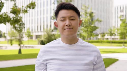 A Young Asian Man Shows a Thumb Down to the Camera and Shakes His Head in an Urban Area