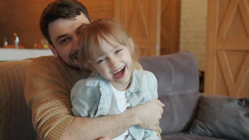 Laughing Father Holding Child on Couch Indoors