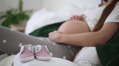Expecting Mother Lying on Bed with Baby Shoes