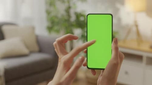 Point of View of Young Woman at Home Living Room Using With Green Mockup Screen Smartphone
