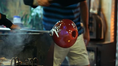 Glassblower Shapes Red Molten Glass in Workshop