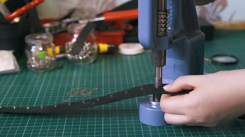 Un ouvrier répare des œillets argentés sur une ceinture en cuir noir