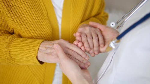 Close-Up Of Doctor Or Nurse Holding Senior Woman Hand At Hospital