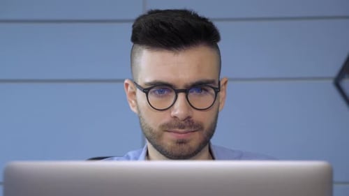 Close Up of A Young European Man with Glasses A Businessman Looking at a Monitor on a Laptop Online
