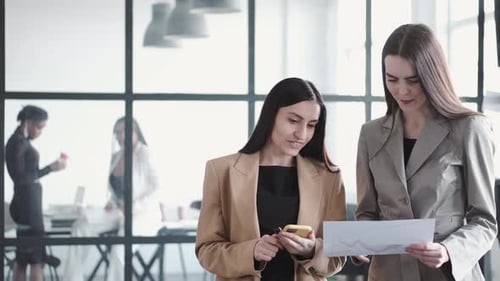 Young Women Reviewing Documents and Phone in Office