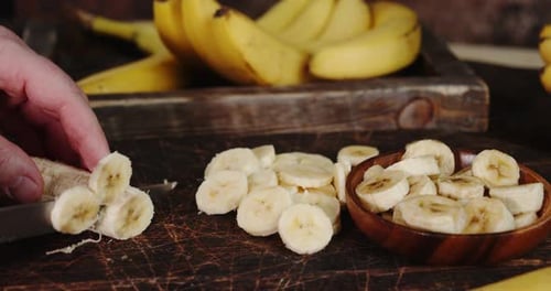Hand Slicing Banana on a Wooden Chopping Board