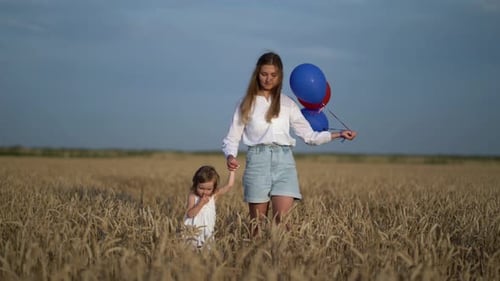 Mother with Daughter and Balloons Walking on Wheat Field