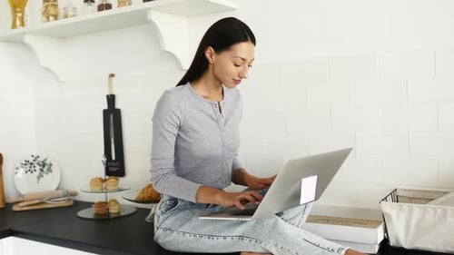 Woman Works on Laptop Sitting on Kitchen Counter